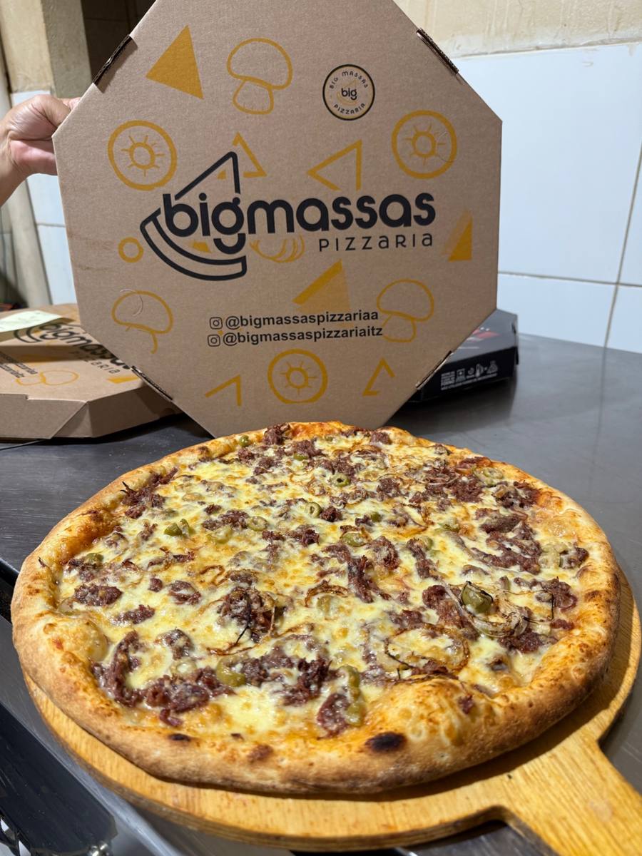 Pizza da Big Massas na pá de madeira, com a caixa da marca ao fundo